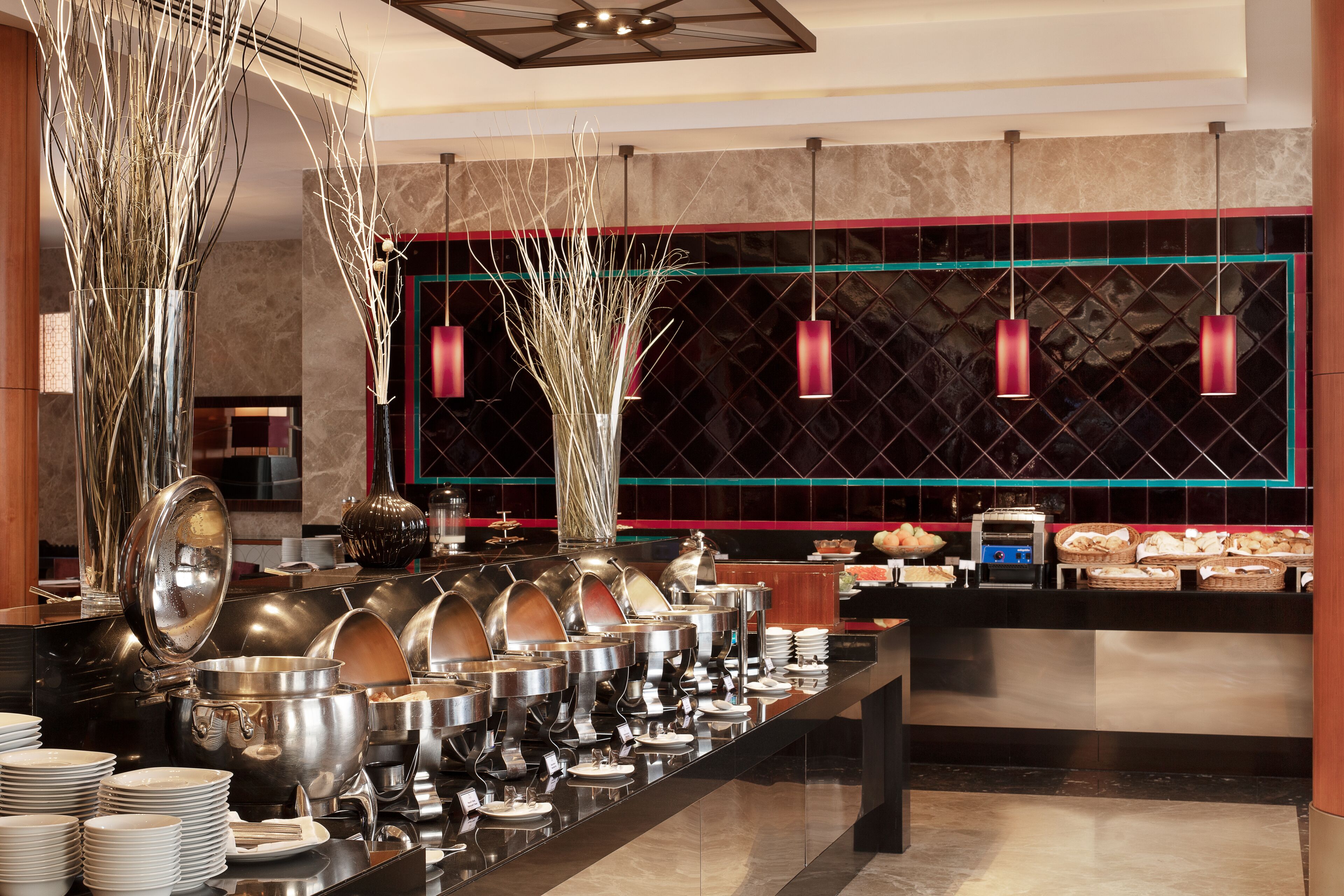 A buffet setup with various food containers and utensils, a counter with baskets, and decorative elements like tall vases and hanging lights.