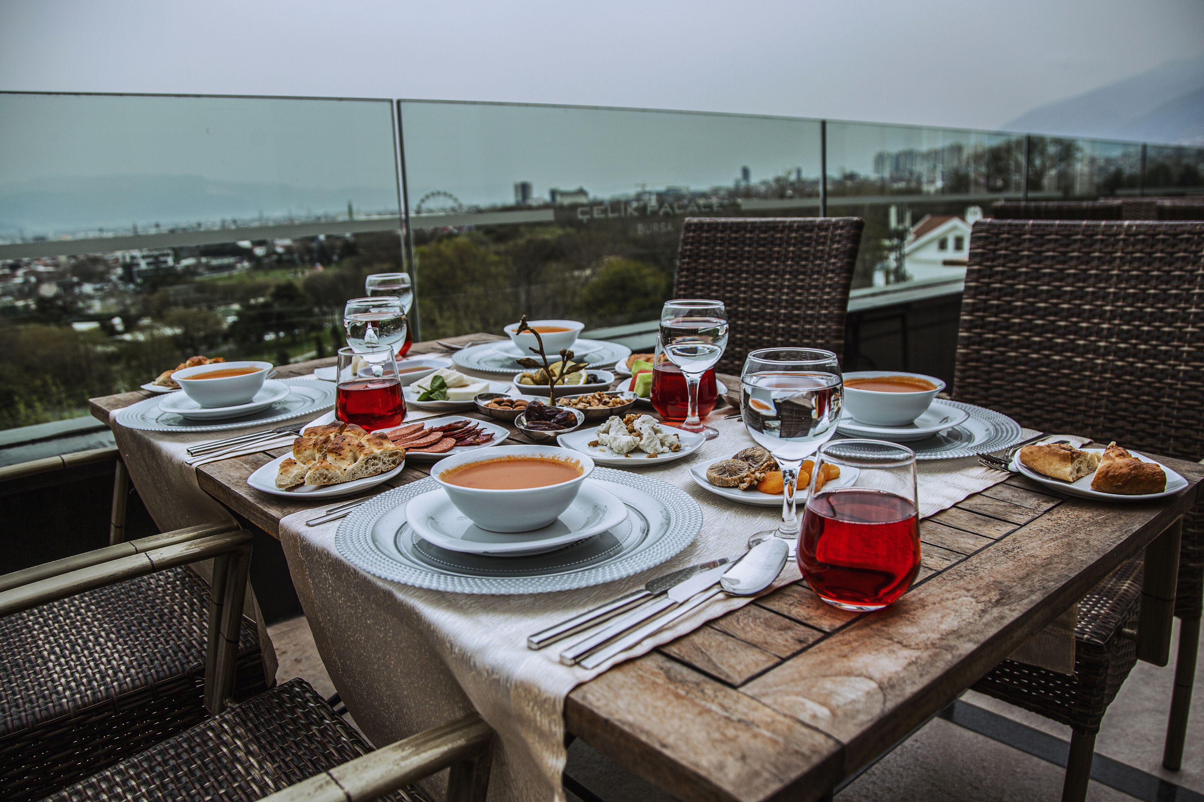 A table set for a meal with various dishes and drinks, overlooking a scenic view.