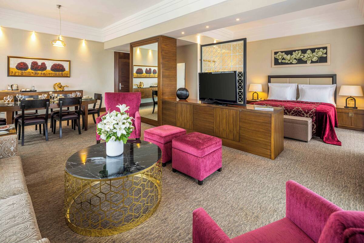 A hotel room with a dining area, a TV, a bed, and a seating area with a coffee table and chairs.