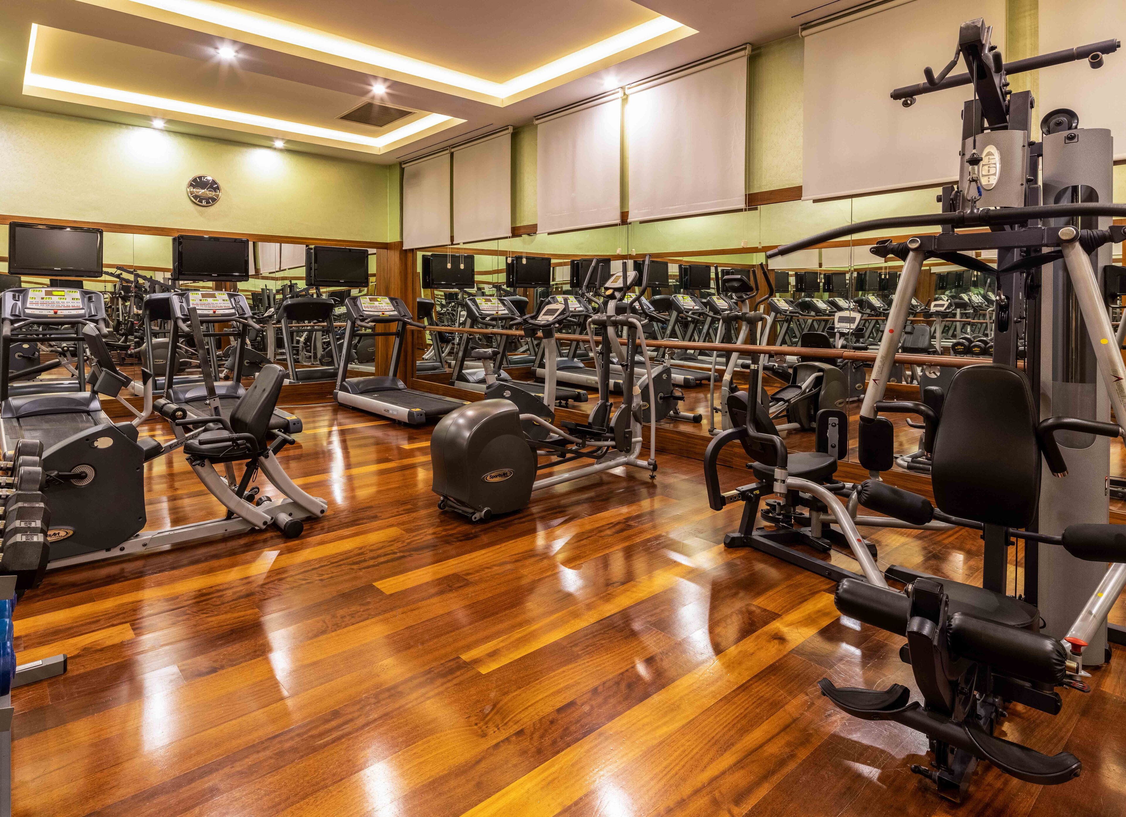 A gym with multiple exercise machines, wooden flooring, and mirrors on the walls.