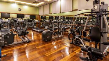 A gym with multiple exercise machines, wooden flooring, and mirrors on the walls.