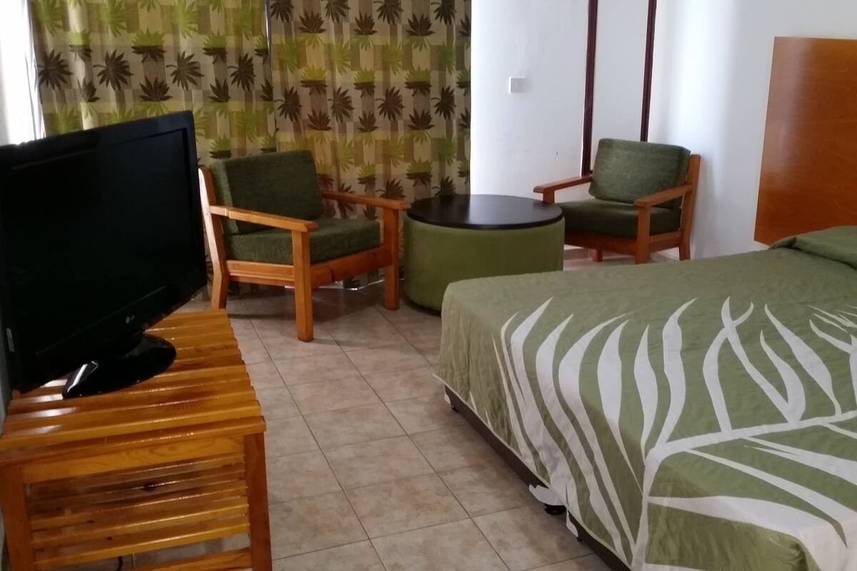 A hotel room with a bed, two chairs, a small round table, and a TV on a wooden stand.