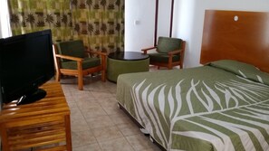 Een hotelkamer met een bed, twee stoelen, een klein rond tafeltje en een televisie op een houten standaard.