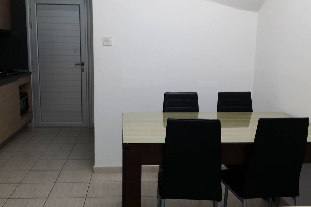 A small, modern kitchen with a dining table and chairs, a refrigerator, and a closed door.