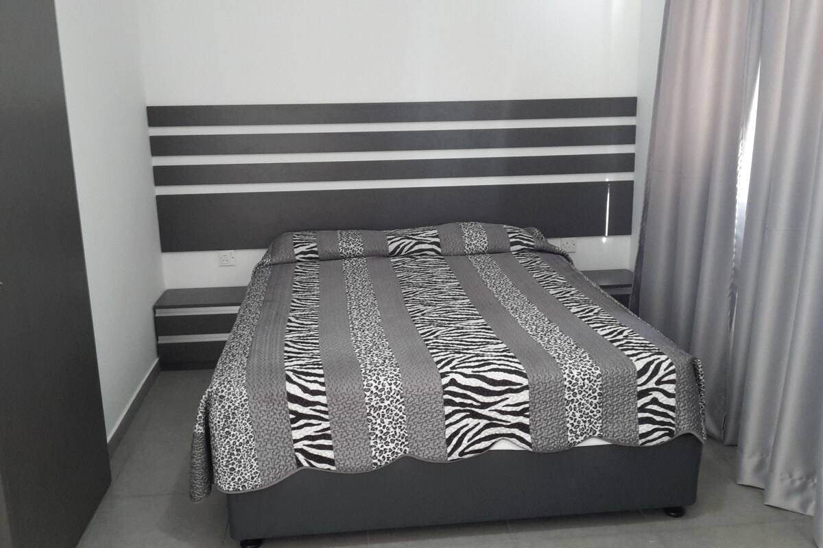A bedroom with a bed, a headboard, a door, and a curtain.