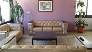 A living room with a beige sofa, a coffee table, and two potted plants. - Agrino Hotel Apartments (Ayia Napa)