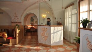 Un vestíbulo de hotel con piso a cuadros, una recepción con un escudo y una zona de estar con un banco.