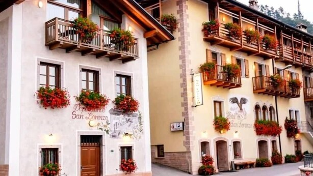 Hotel con balcones decorados con flores y un letrero que dice 'Hotel San Lorenzo', con un estilo arquitectónico tradicional.