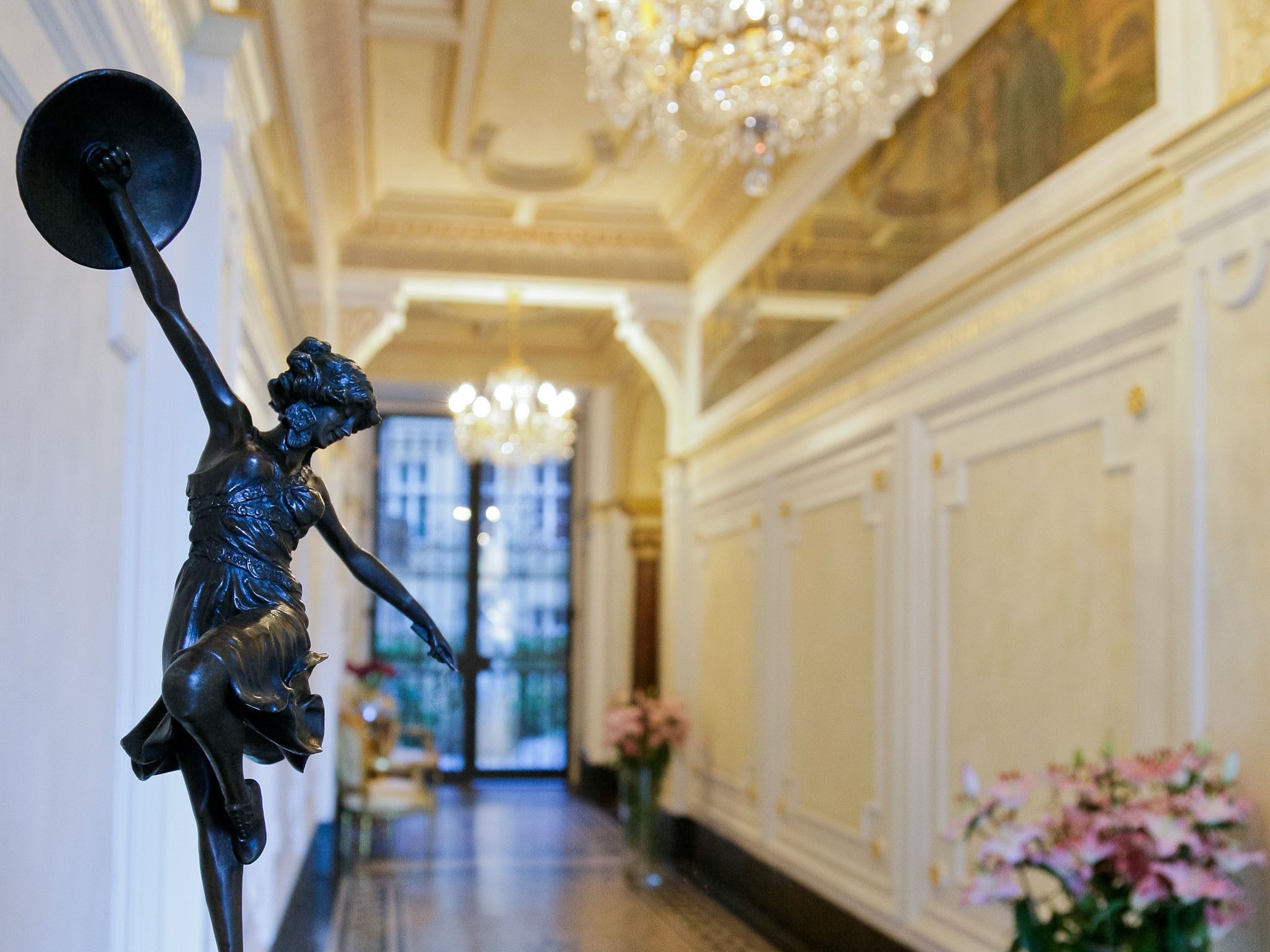 Un amplio pasillo con una estatua, candelabros y arreglos florales.