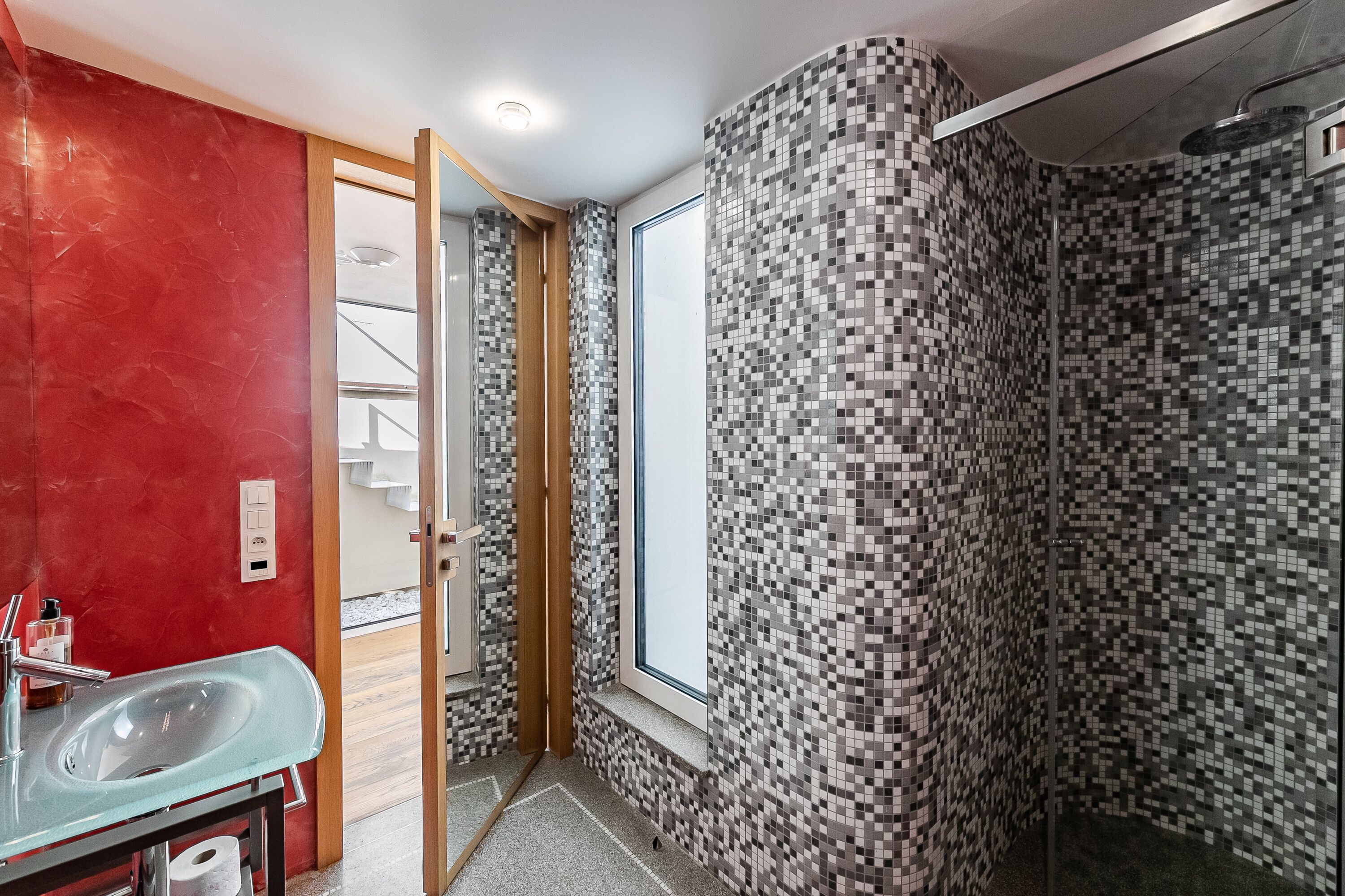 Ein Badezimmer mit einem Glaswaschbecken, roten Wänden und einer Dusche mit Mosaikfliesen.
