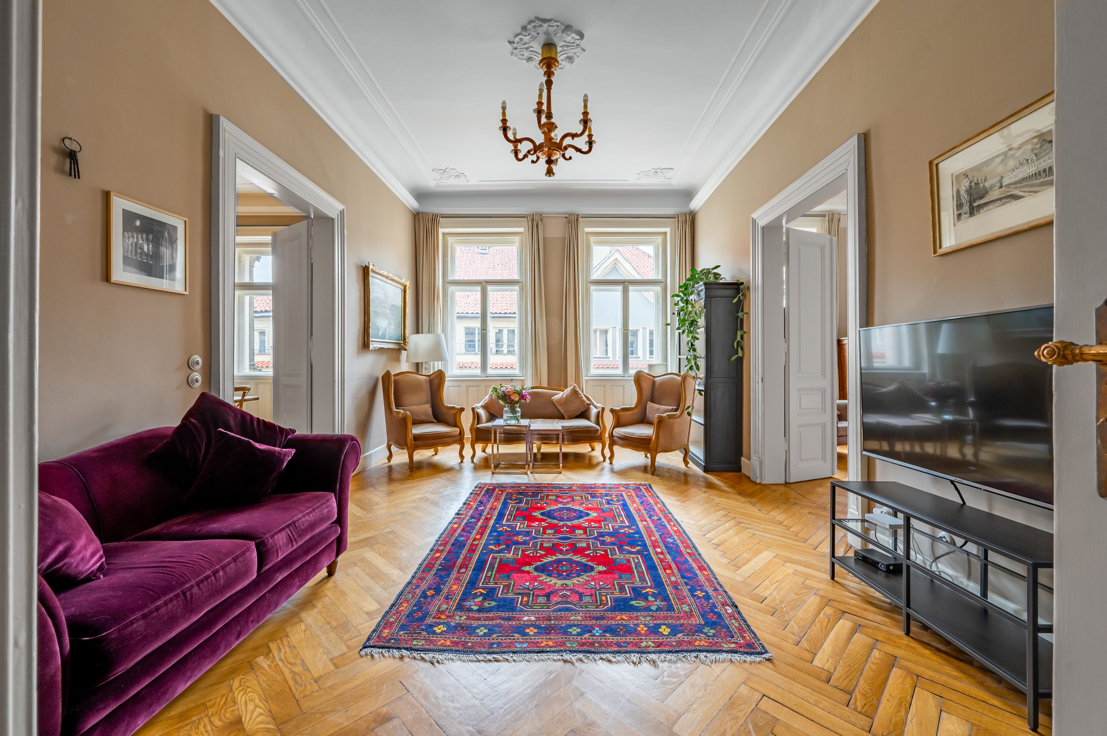 Un salon avec un canapé violet, un téléviseur, un lustre et un tapis à motifs.