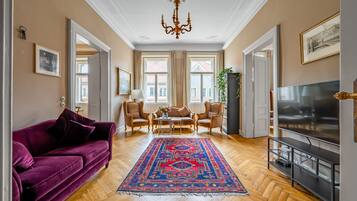 Un salon avec un canapé violet, un téléviseur, un lustre et un tapis à motifs.