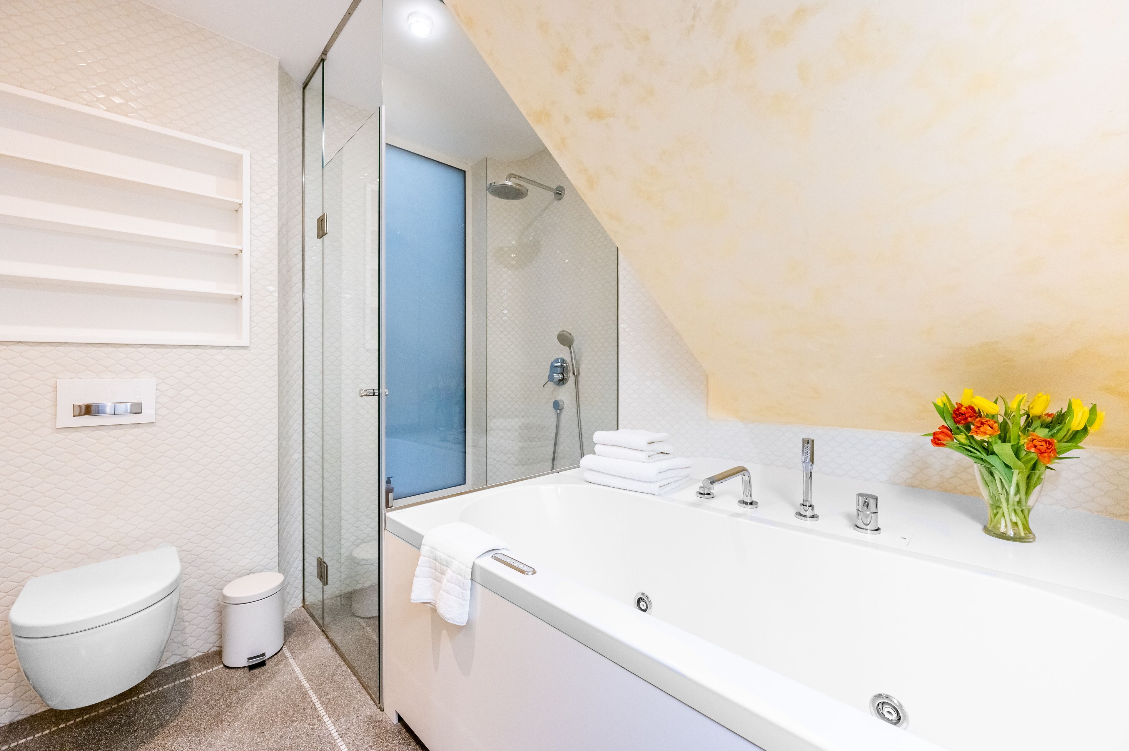 A modern bathroom with a large bathtub, a glass shower enclosure, a toilet, and a sink with a vase of flowers.