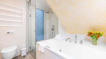 A modern bathroom with a large bathtub, a glass shower enclosure, a toilet, and a sink with a vase of flowers.