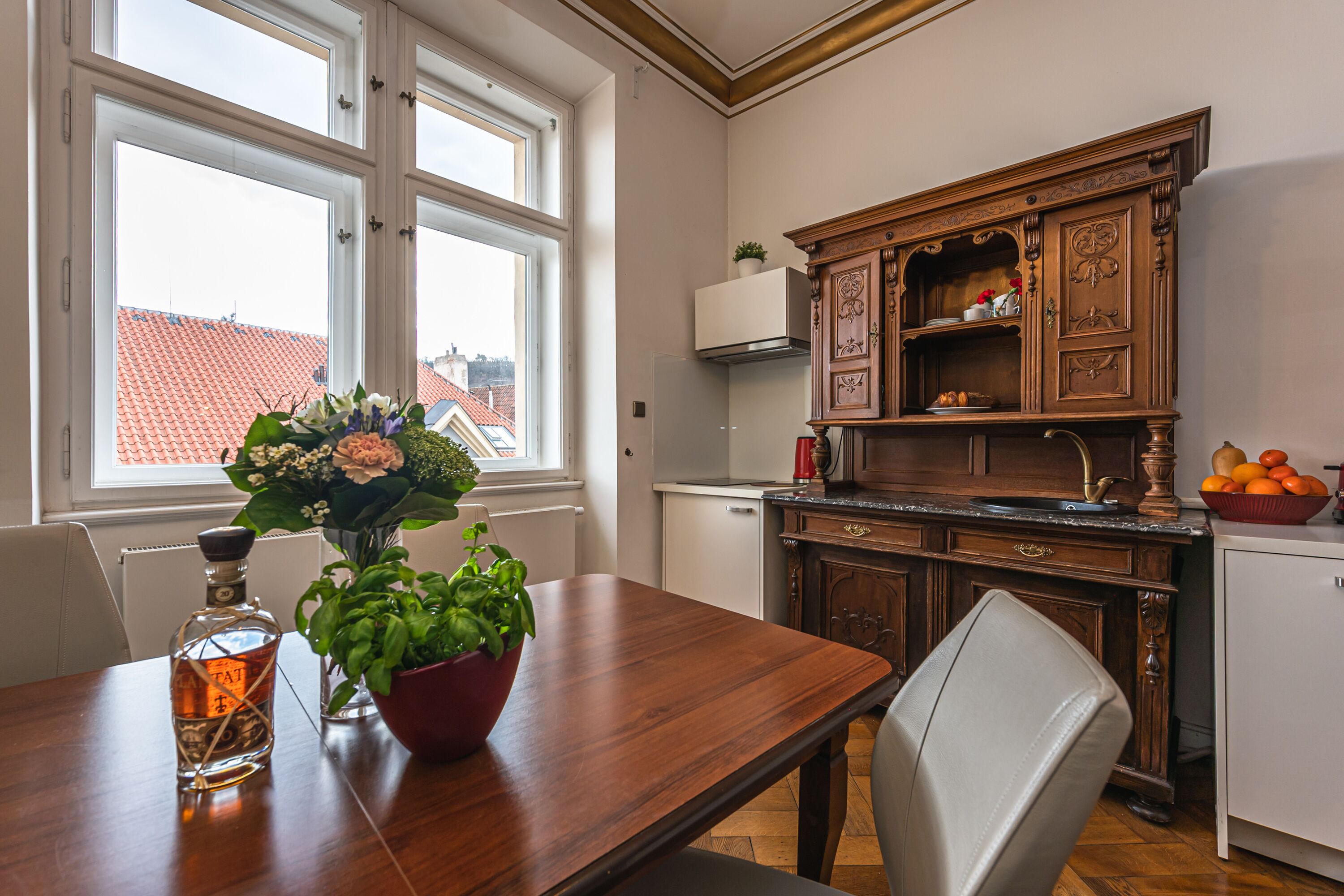 A dining area with a wooden table, chairs, a vase with flowers, and a bottle of liquor.