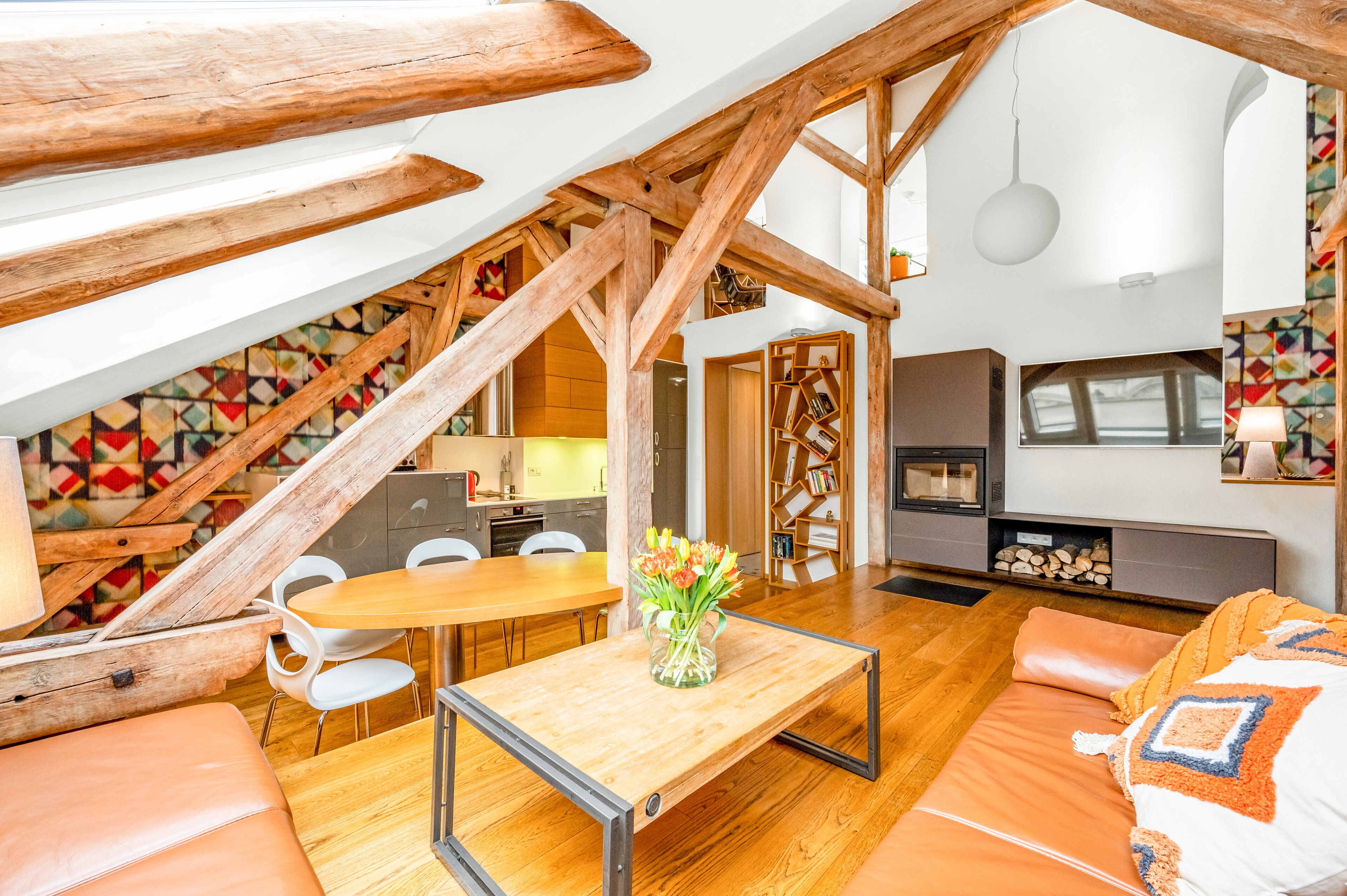 Un loft espacioso con vigas de madera a la vista, un comedor con mesa y sillas de madera, un sofá y una estantería.