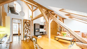 Un loft espacioso con una zona de comedor de madera, sillas blancas, un sofá y un televisor.