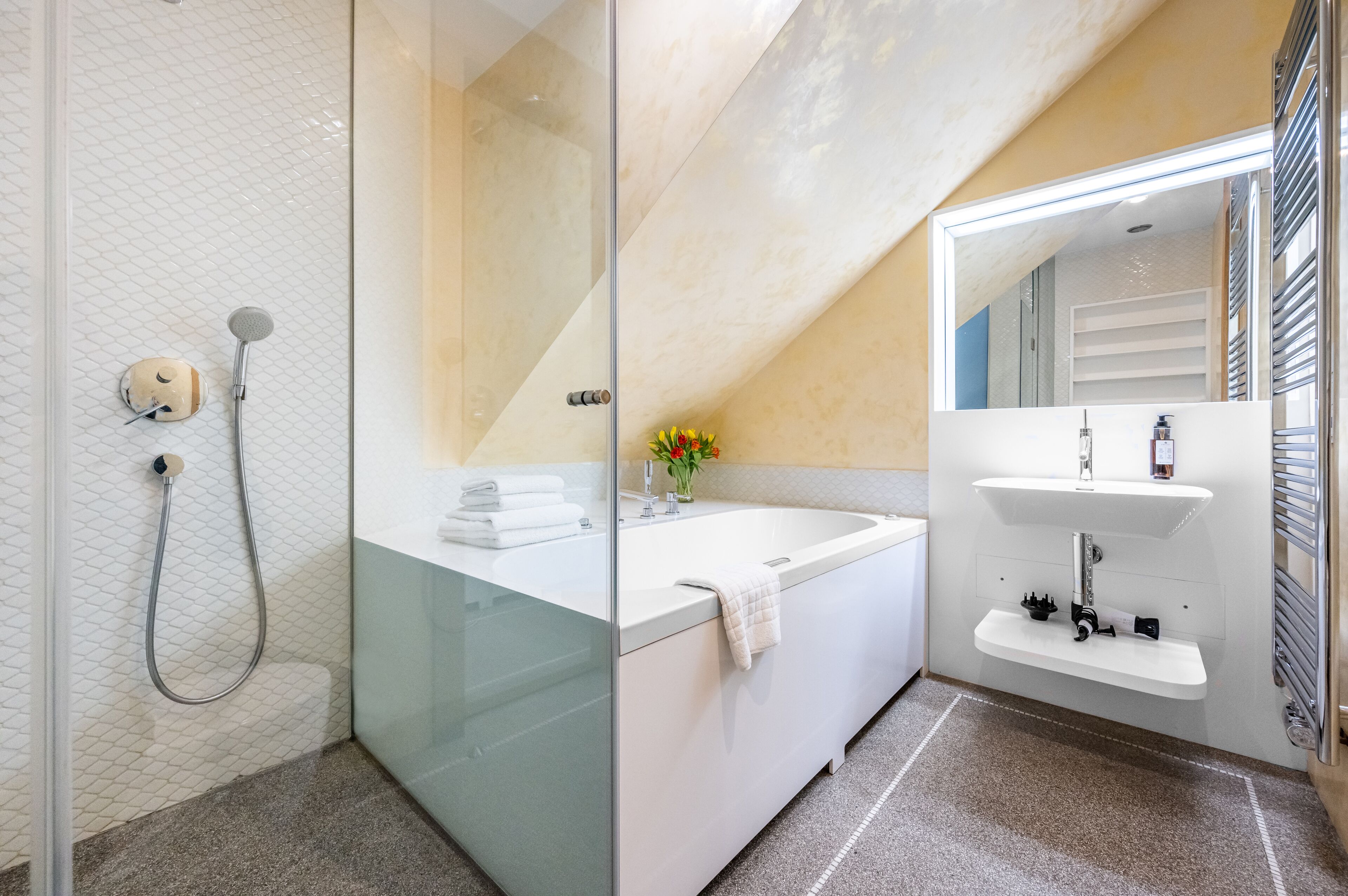 A modern bathroom with a glass-enclosed shower, a white bathtub, and a vanity with a mirror.