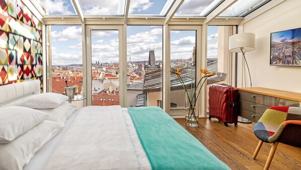 A bedroom with a large bed, a glass table, a vase with flowers, a red suitcase, and a colorful chair. - Malostranska Residence (Prague)