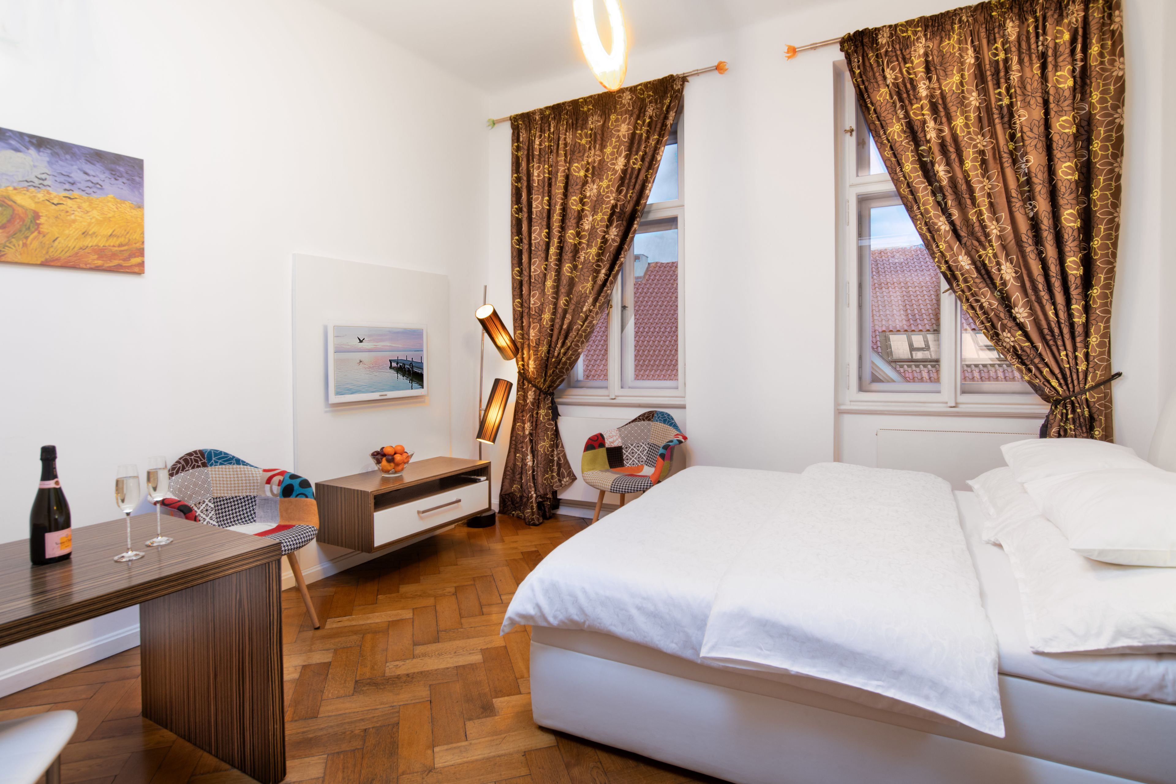 Een slaapkamer met een bed, een bureau met een fles en glazen, een stoel en gordijnen.