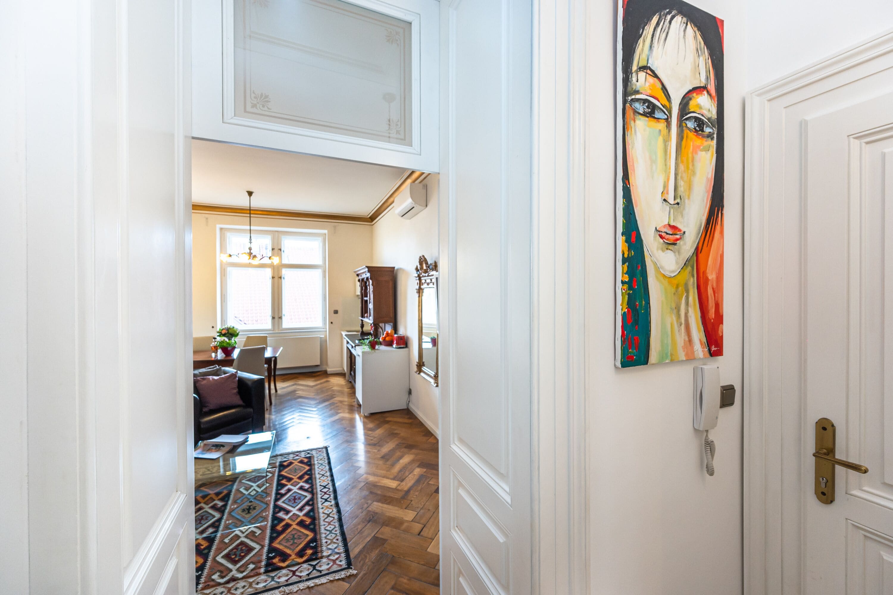 A hallway with a patterned rug, a painting on the wall, and a door with a brass handle.