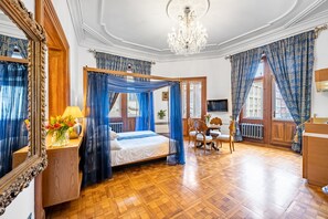 A bedroom with a four-poster bed, wooden floor, chandelier, and large windows with blue curtains. - Malostranska Residence (Prague)