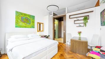 A modern bedroom with a large bed, a wooden side table, a chair, and a small table with a vase of flowers.