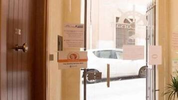 Entrada de un hotel con puerta de madera, puerta de vidrio y un coche a la vista.