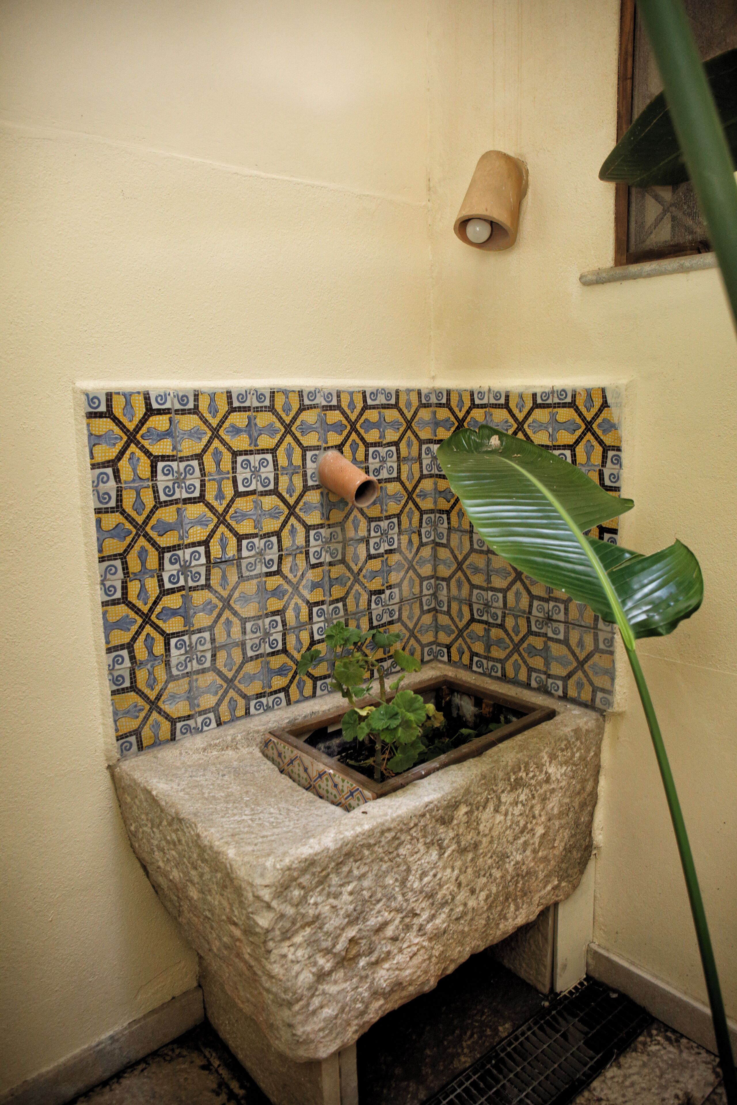 A bathroom with a tiled wall, a stone sink, and a potted plant.