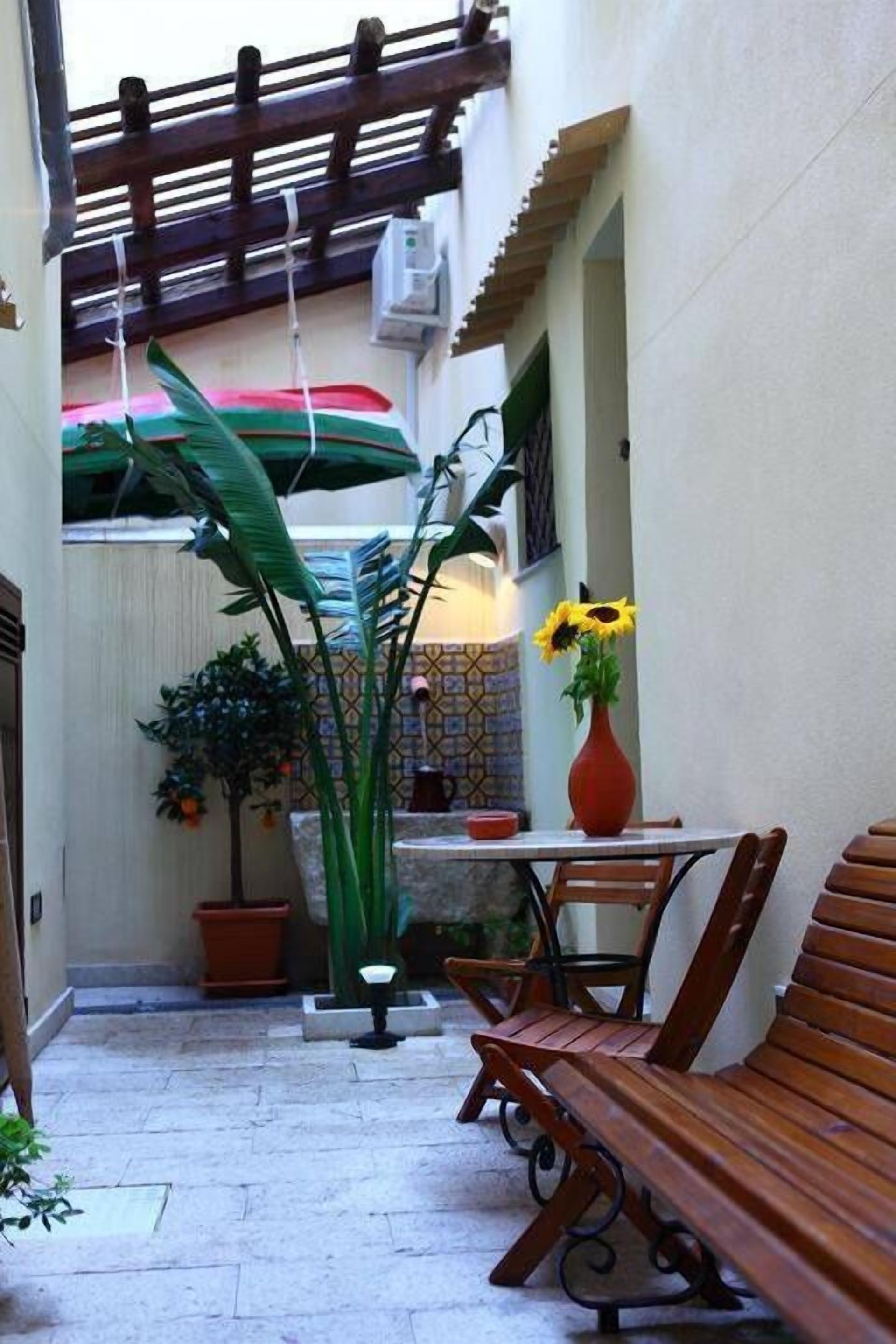 Um pátio externo estreito com um banco de madeira, uma mesa e um vaso de planta.