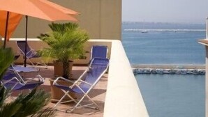 Un balcón con dos sillones de descanso y una sombrilla, con vistas a una piscina y el océano.