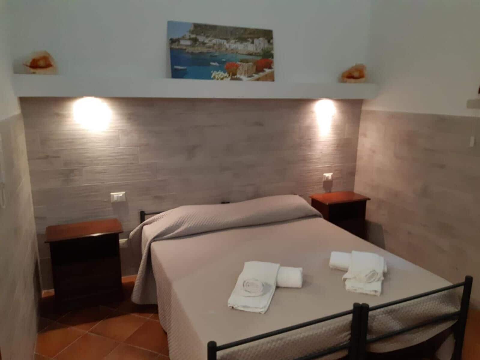 Une chambre à coucher avec un lit, deux tables de chevet, une commode, un tableau au-dessus du lit et un sol carrelé.