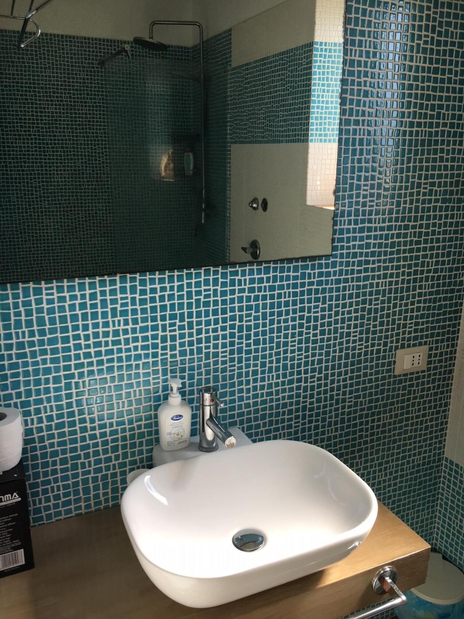 Ett badrum med ett vitt handfat, en spegel ovanför och en vägg täckt med kakel.