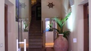 Un pasillo con puerta de vidrio, un jarrón grande y una escalera que sube a un nivel superior.
