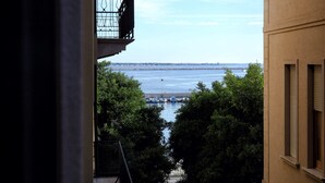 Vista desde un balcón sobre un cuerpo de agua con barcos, árboles y un puente distante.