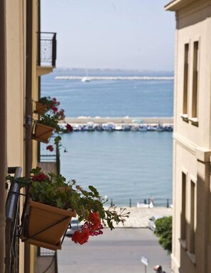 A balcony with hanging flower baskets and a view of the sea and boats. - Palazzo dei Corsari- Apartment (Trapani)