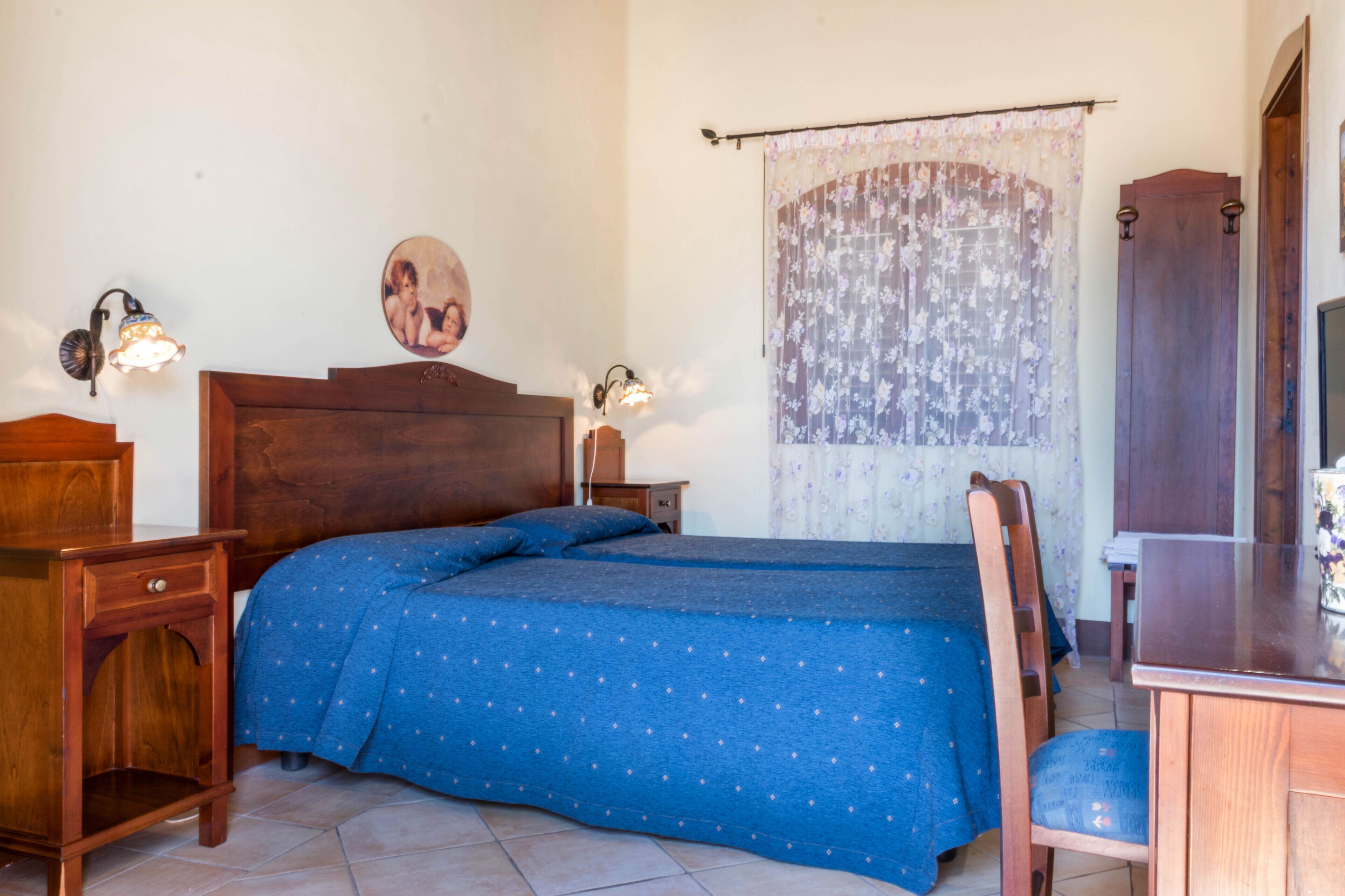 Een slaapkamer met een houten bed, twee nachtkastjes, een stoel, een bureau en een gordijn.