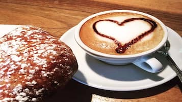 Uma chávena de café com um desenho de coração no espuma, um pastel e uma mesa de madeira.