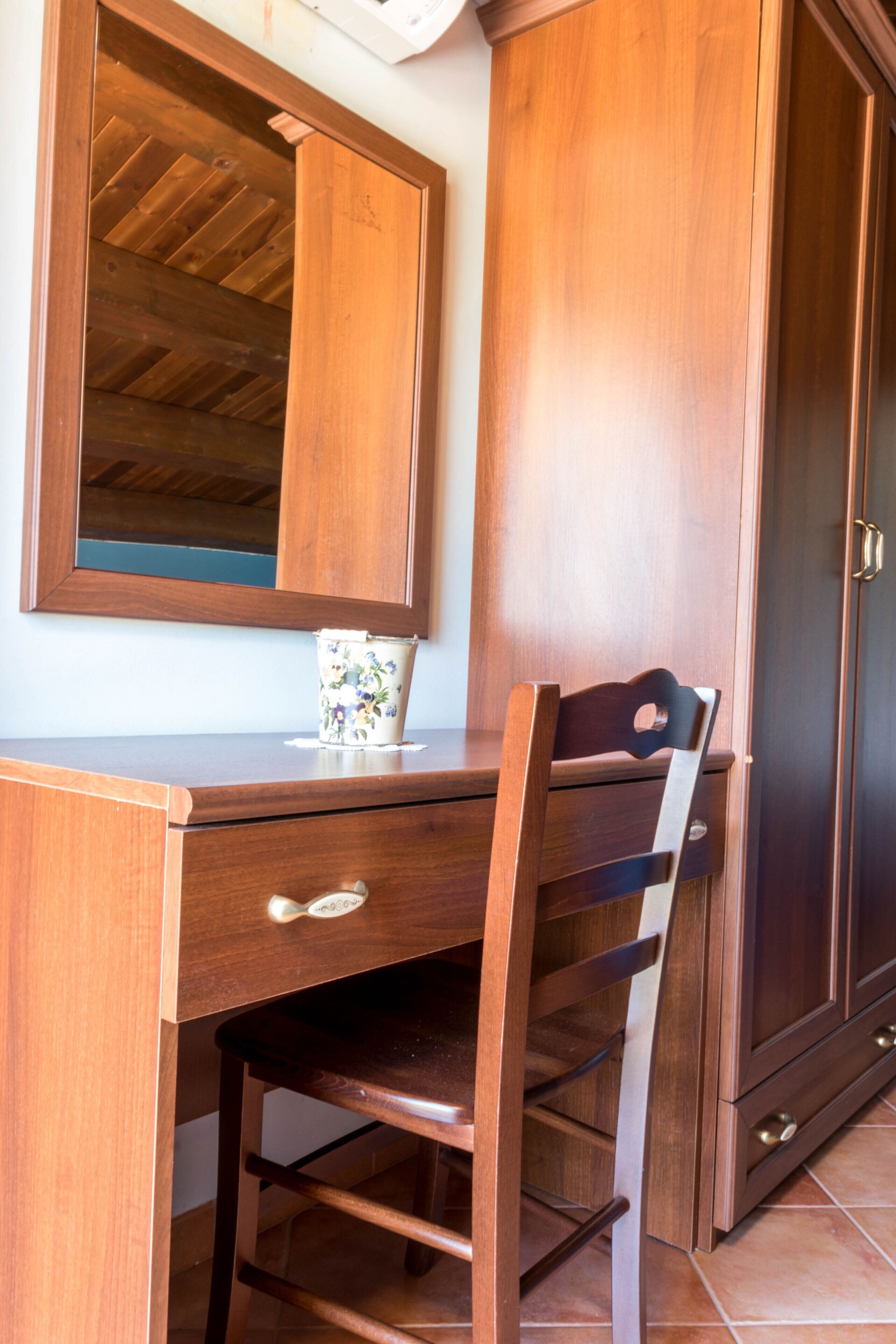 A wooden desk with a chair, a cabinet, and a mirror.