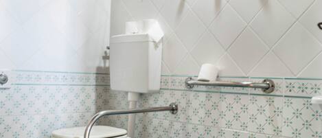 A bathroom with a toilet, bidet, and sink, featuring blue tiles and a wooden towel rack.