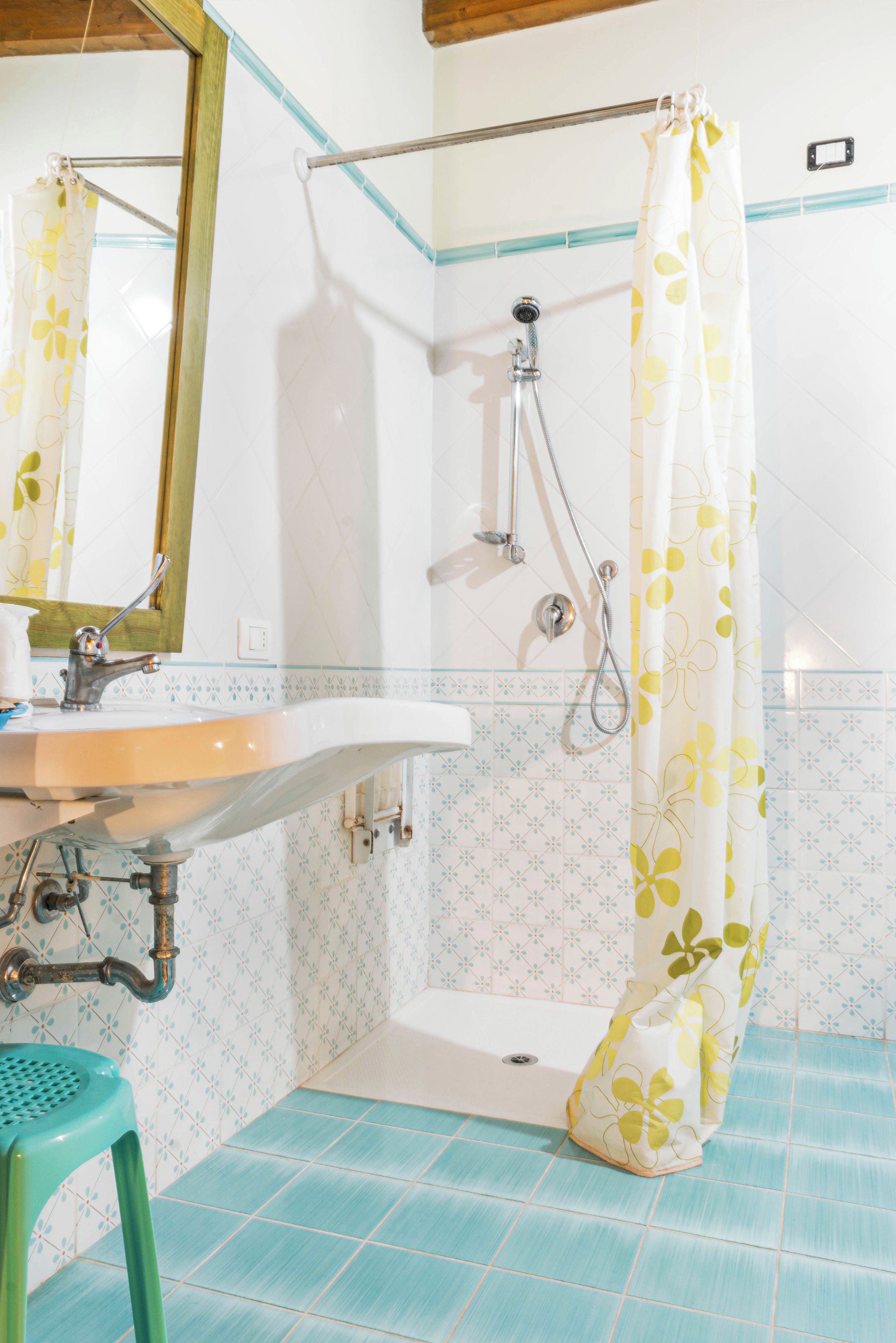 A bathroom with a sink, mirror, shower, and a green stool.