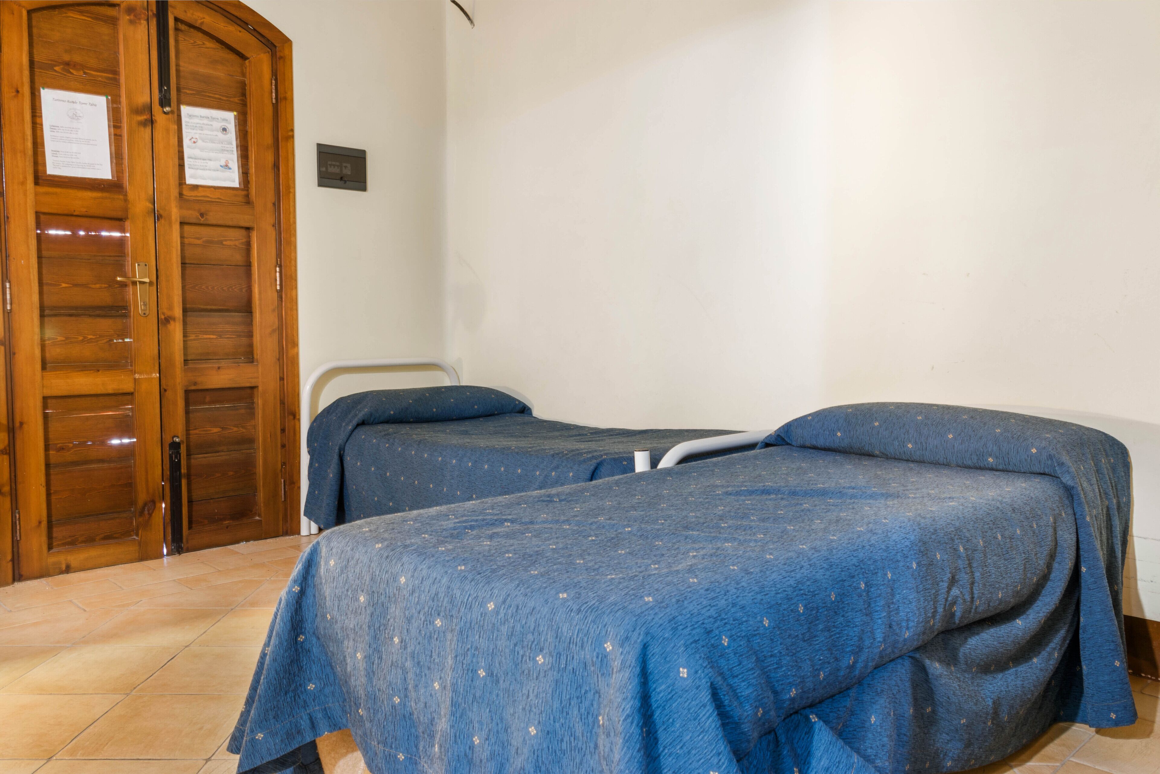 Ein Zimmer mit zwei Einzelbetten, einer Holztür und einem Fliesenboden.