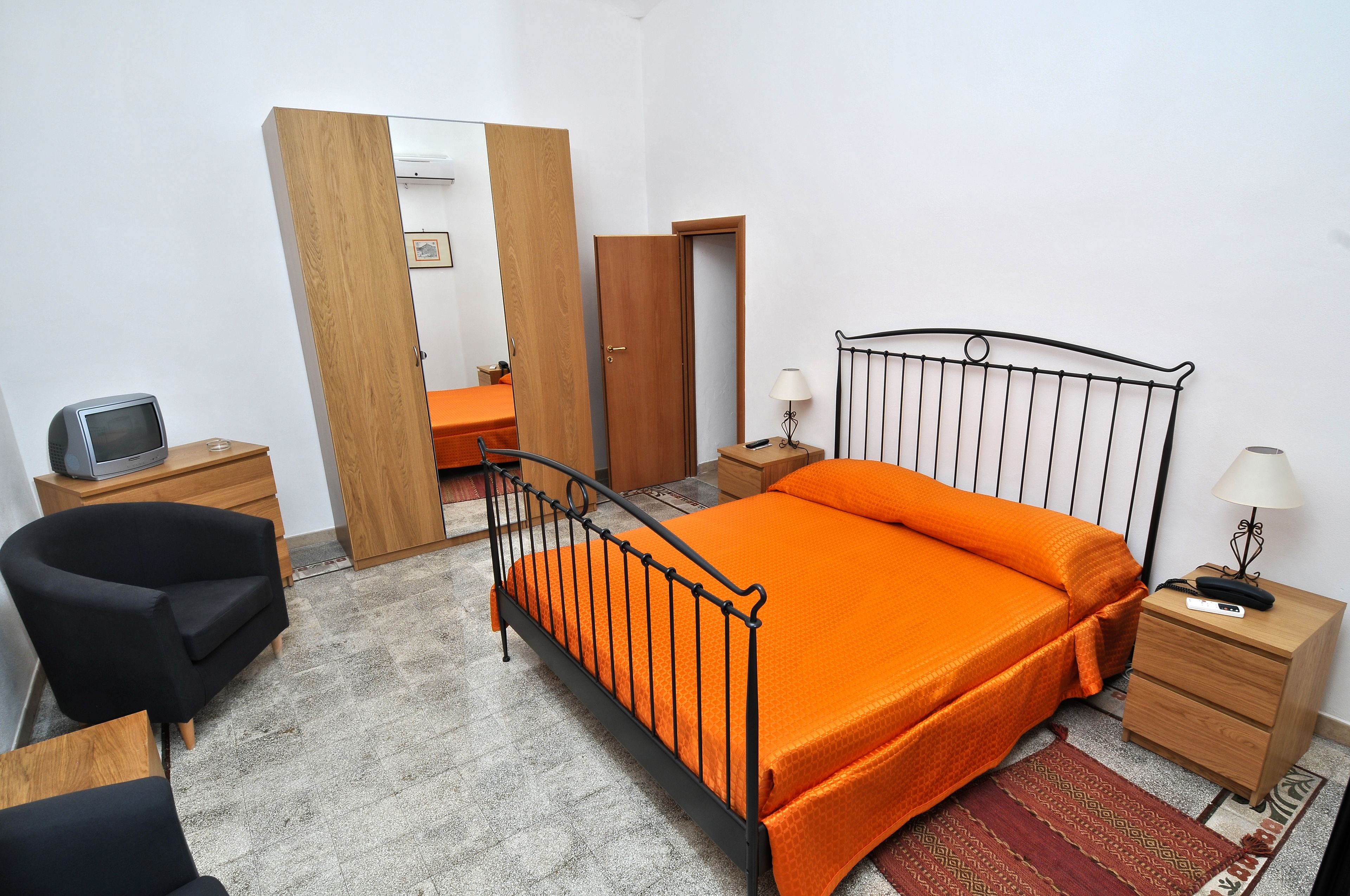 A bedroom with a bed, a chair, a desk, a wardrobe, and a mirror.