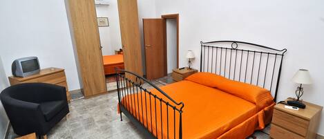 A bedroom with a bed, a chair, a desk, a wardrobe, and a mirror.