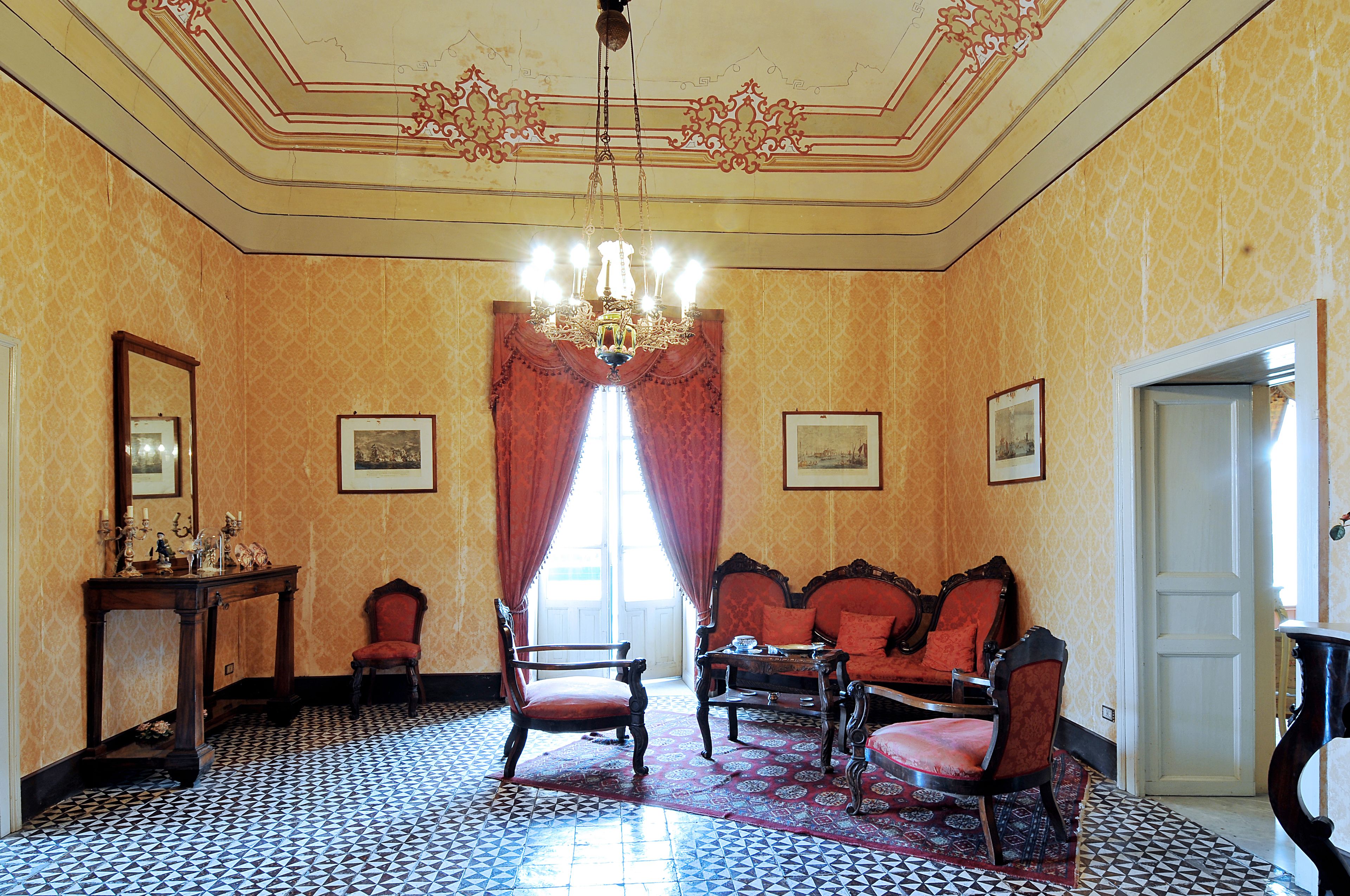 A room with a patterned floor, a chandelier, a red sofa set, and a wooden chair.