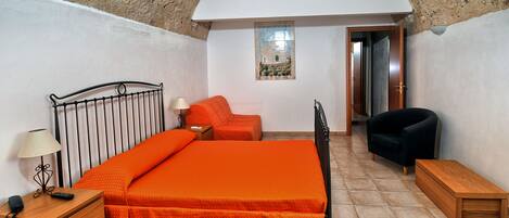 Un dormitorio con cama, mesita de noche, lámpara, silla y una pequeña mesa.