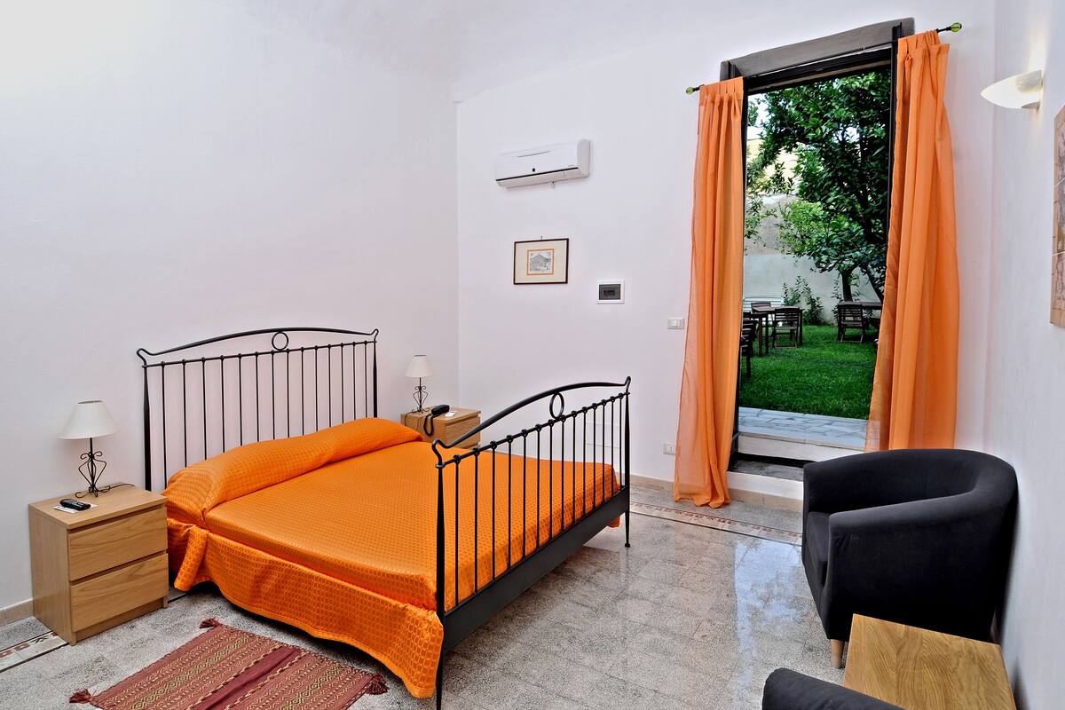 A bedroom with a bed, nightstand, lamp, and a view of an outdoor area with a table and chairs.