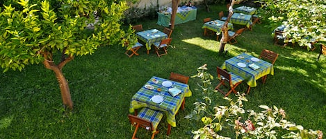 Un jardín exterior con varias mesas y sillas, rodeado de abundante vegetación y árboles.