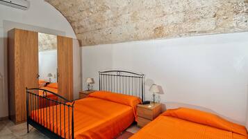 A bedroom with a rustic stone ceiling, two beds with orange bedding, wooden wardrobe, and bedside lamps.