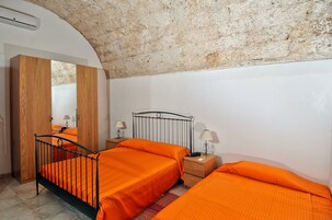 Un dormitorio con techo de piedra rústica, dos camas con ropa de cama naranja, un armario de madera y lámparas de noche.